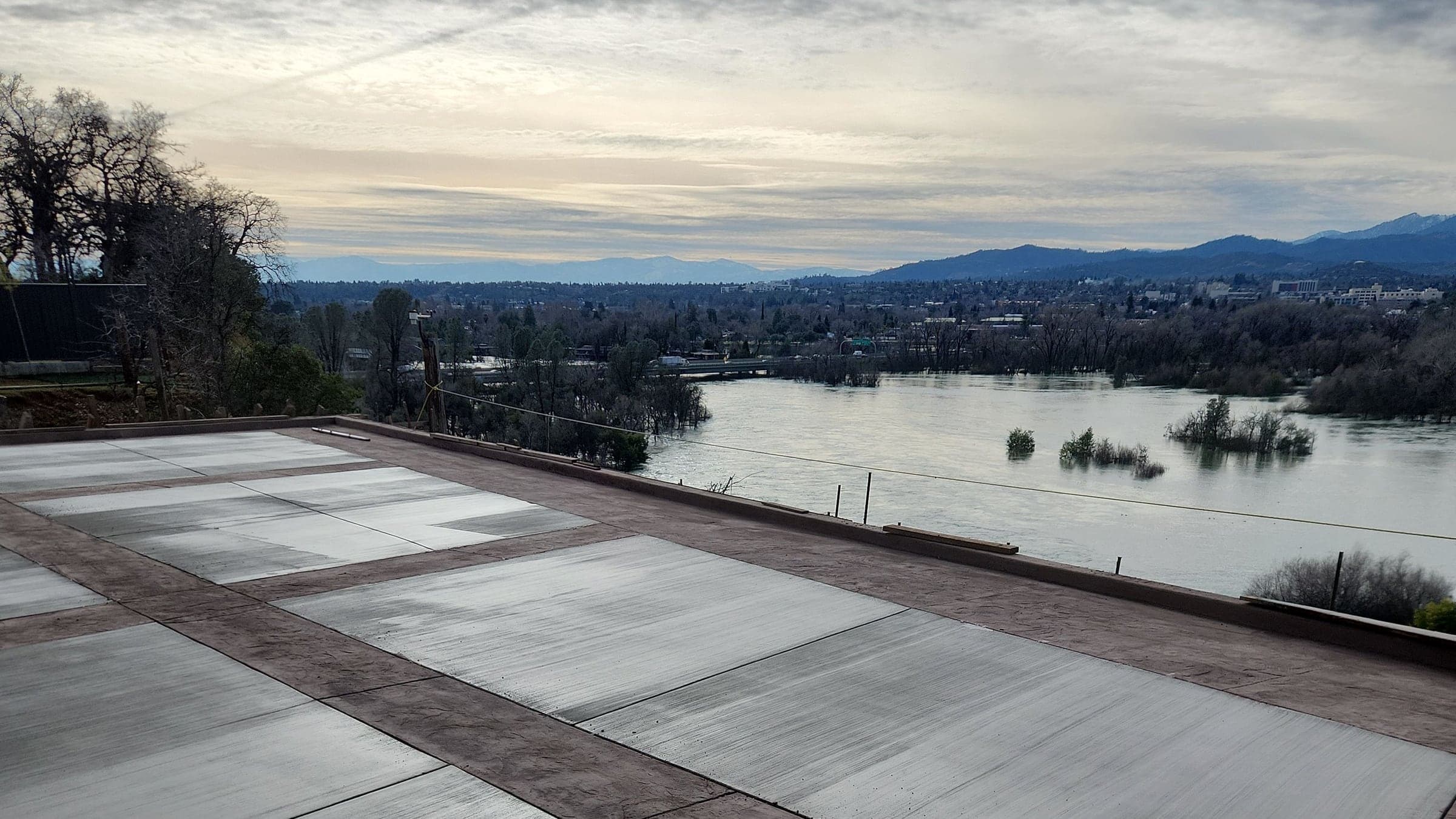 A banded concrete patio on a bluff above the Sacramento River, with Redding and the mountains beyond at dusk