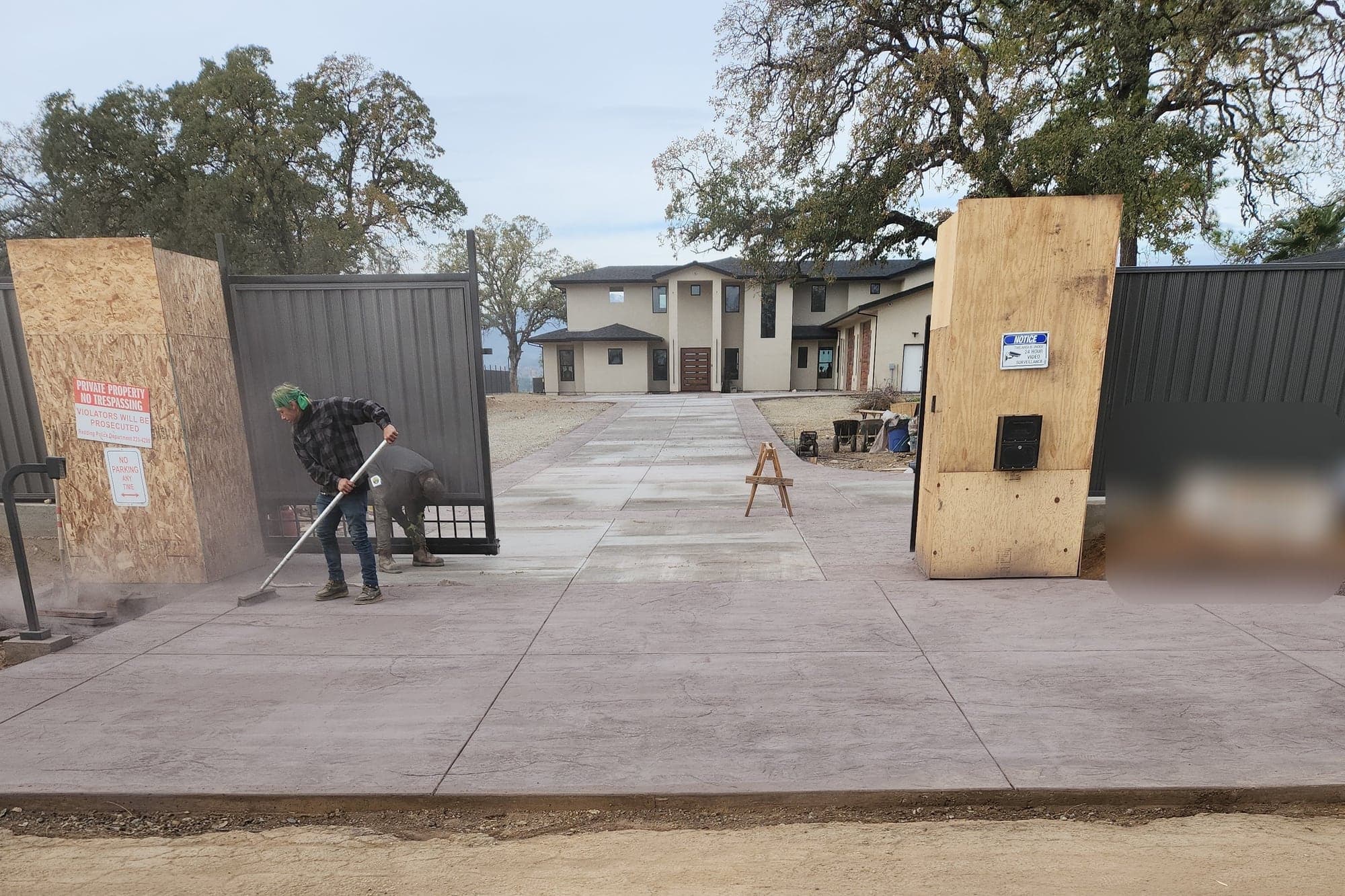 A finished textured and colored concrete driveway running from a gated entry up to a new two-story home