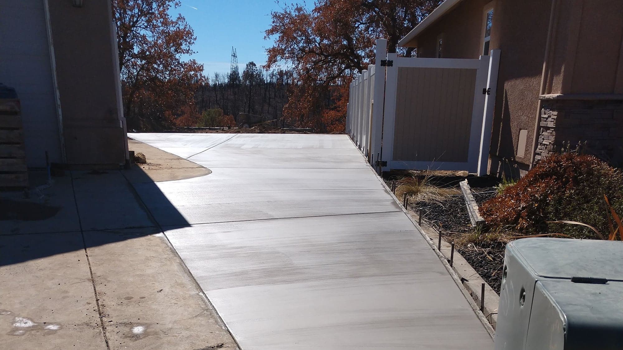 A finished concrete side approach running between a house and a fence line, joining the existing driveway