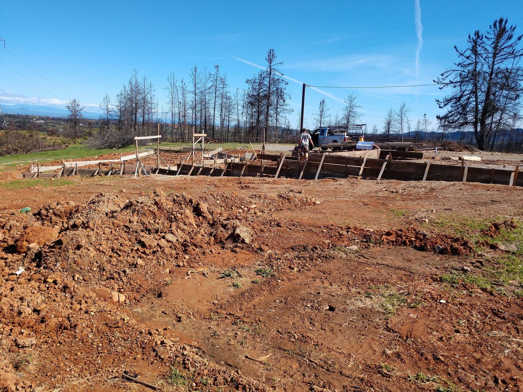 The building footprint formed and braced on cleared ground with standing burned timber beyond