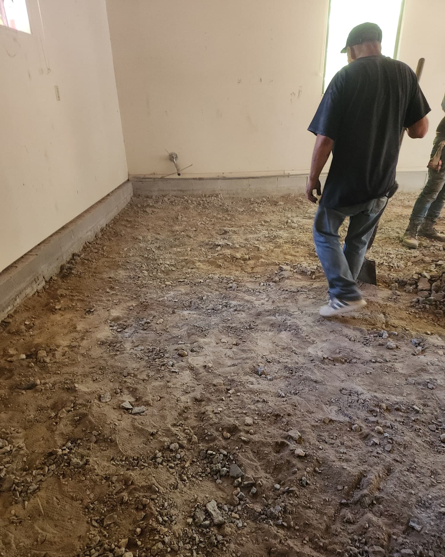 An S & L Concrete crew member crossing a torn-out interior floor, shovel in hand, before the new slab goes down